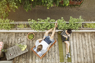 Young couple relaxing on their balcony in summer, man using tablet - PESF01097