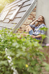 Happy young man sitting on his balcony, relaxing - PESF01100