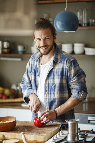 Junger Mann bei der Zubereitung von Essen zu Hause, Schneiden von Gemüse, lizenzfreies Stockfoto