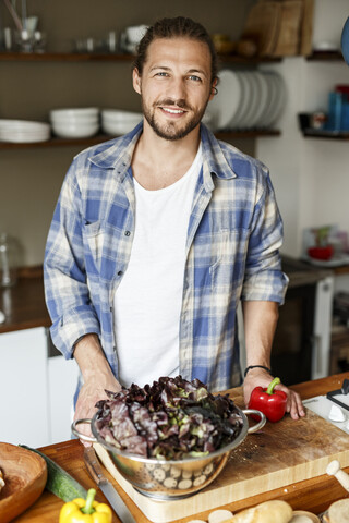 Junger Mann bei der Essenszubereitung zu Hause, Reinigung von Salat, lizenzfreies Stockfoto