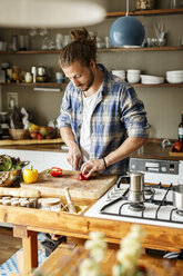 Young man preparing food at home, slicing vegetables - PESF01114