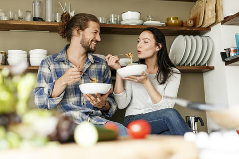 Glückliches Paar sitzt in der Küche und isst Spaghetti, lizenzfreies Stockfoto