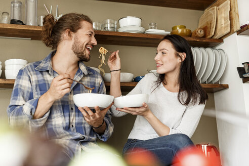 Happy couple sitting in kitchen, eating spaghetti - PESF01128