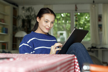 Junge Frau sitzt zu Hause und benutzt ein digitales Tablet - PESF01133