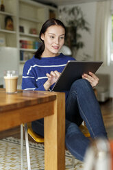 Junge Frau sitzt zu Hause und benutzt ein digitales Tablet - PESF01137