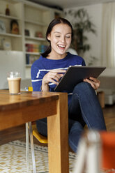 Junge Frau sitzt zu Hause und benutzt ein digitales Tablet - PESF01138