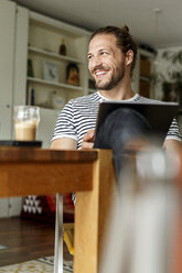 Young man with a bun sitting at home, using tablet - PESF01141