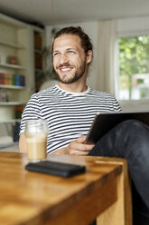 Junger Mann mit Brötchen sitzt zu Hause und benutzt ein digitales Tablet - PESF01142