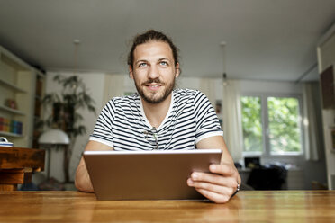 Young man with a bun sitting at home, using digital tablet - PESF01148