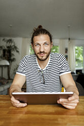 Young man with a bun sitting at home, using digital tablet - PESF01149