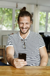 Young man with a bun sitting at home, using smartphone - PESF01152