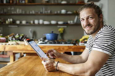 Young man with a bun sitting at home, using digital tablet - PESF01155
