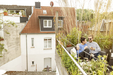 Young couple relaxing on their balcony, sitting on couch - PESF01158