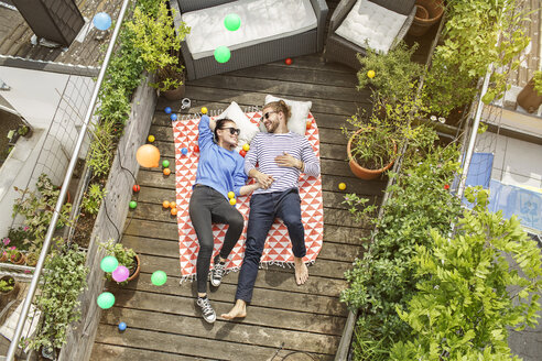 Junges Paar entspannt sich auf dem Balkon, auf einer Decke liegend, die Arme um sich gelegt - PESF01171
