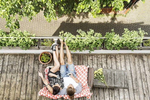 Young couple relaxing on their balcony in summer, drinking coffee - PESF01180