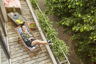 Young woman sitting in deck chair, relaxing on her balcony - PESF01187