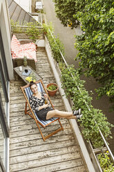 Young woman sitting in deck chair, relaxing on her balcony - PESF01188