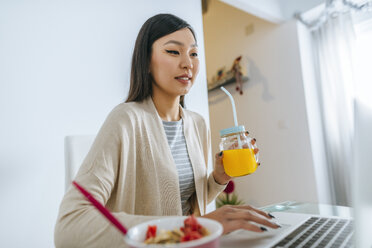 Junge Frau frühstückt, während sie am Laptop arbeitet - KIJF02263