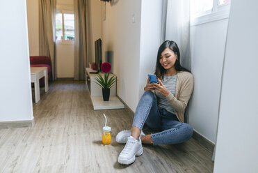 Young woman sitting on floor, using smartphone - KIJF02267