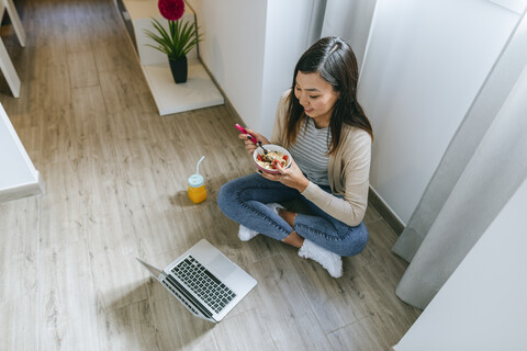 Junge Frau sitzt auf dem Boden und benutzt ein Smartphone, lizenzfreies Stockfoto