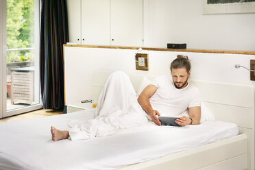 Junger Mann liegt auf dem Bett und benutzt ein digitales Tablet am Morgen - PESF01220