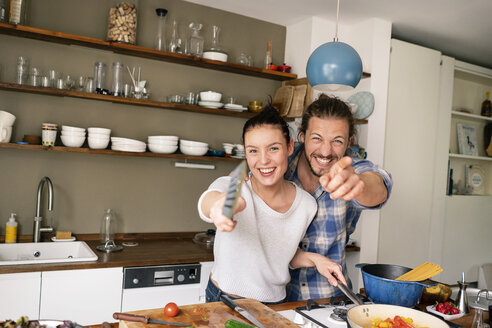 Junges Paar, das gemeinsam Essen zubereitet, lachend und mit dem Spatel zeigend - PESF01230