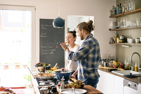 Young couple preparing food together, tasting spaghetti - PESF01240