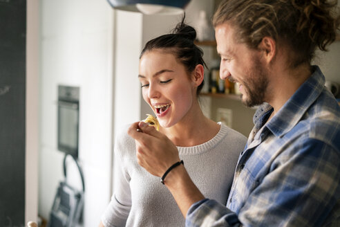 Young couple preparing food together, tasting spaghetti - PESF01241