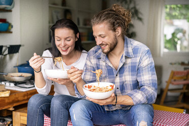 Happy couple sitting on kitchen table, eating spaghetti - PESF01244