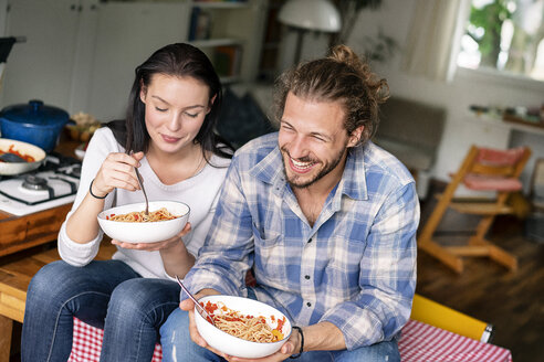 Happy couple sitting on kitchen table, eating spaghetti - PESF01245
