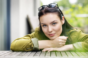 Portrait of a young woman, with sunglasses in her hair, sitting at outdoor table - PESF01252