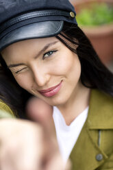 Portrait of a young woman with cap, winking and pointing - PESF01257