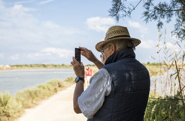 Italien, Sizilien, Naturschutzgebiet Vendicari, älterer Mann, der ein Smartphone-Foto macht - MAMF00375