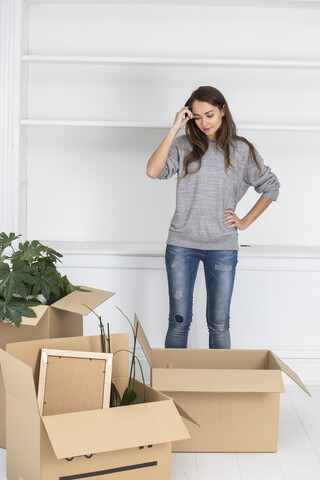 Frau steht mit Kartons im neuen Haus, lizenzfreies Stockfoto