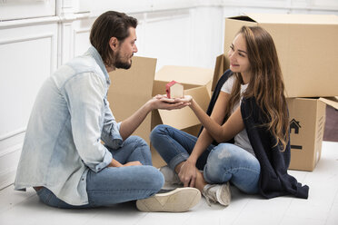 Man handing over tiny house model to girlfriend surrounded by cardboard boxes - ERRF00765