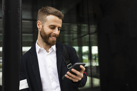 Lächelnder stilvoller Geschäftsmann beim Telefonieren in der Stadt, lizenzfreies Stockfoto