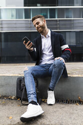 Stylish businessman sitting in the city using cell phone - JRFF02587