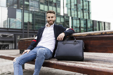 Portrait of smiling stylish businessman sitting on a bench in the city - JRFF02590