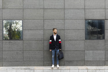 Stilvoller Geschäftsmann steht vor einer grauen Wand und schaut sich um - JRFF02594