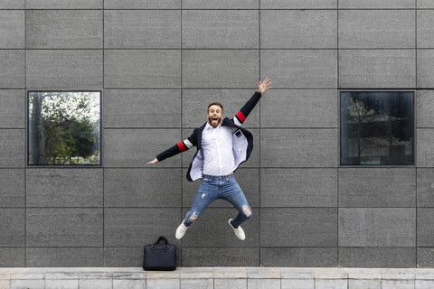 Aufgeregter Geschäftsmann springt vor ein Gebäude, lizenzfreies Stockfoto