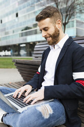 Stilvoller Geschäftsmann sitzt auf einer Bank in der Stadt und benutzt einen Laptop - JRFF02597