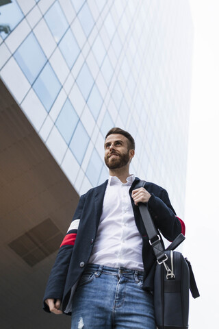 Stilvoller Geschäftsmann vor einem Bürogebäude, der sich umschaut, lizenzfreies Stockfoto