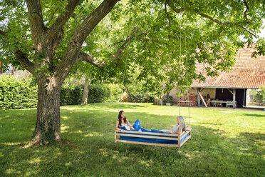 Two women relaxing on a hanging bed in garden - PESF01260