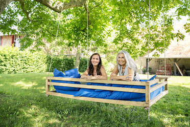 Porträt von zwei lächelnden Frauen, die sich auf einem Hängebett im Garten entspannen - PESF01261