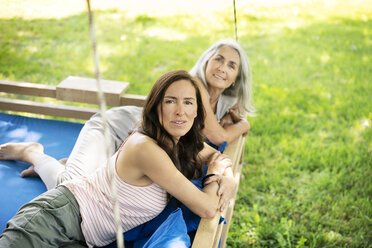Portrait of two smiling women relaxing on a hanging bed in garden - PESF01262