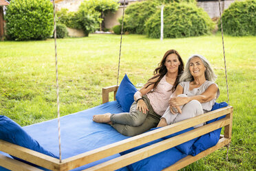 Porträt von zwei lächelnden Frauen, die sich auf einem Hängebett im Garten entspannen - PESF01263