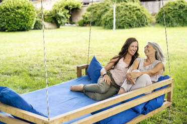Two happy women relaxing on a hanging bed in garden - PESF01265