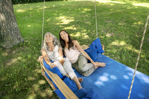 Zwei Frauen entspannen sich auf einem Hängebett im Garten und schauen nach oben - PESF01268