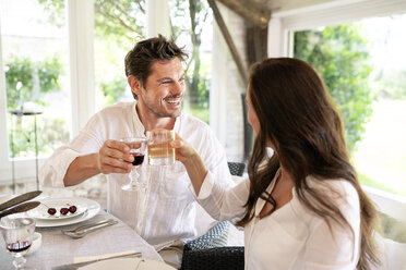 Happy couple clinking glasses at dining table - PESF01284