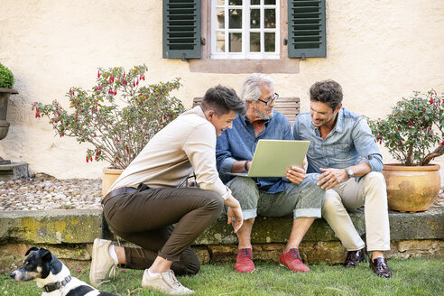 Drei glückliche Männer unterschiedlichen Alters benutzen einen Laptop im Garten - PESF01295